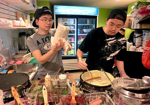 正忙着摊煎饼的两个留学生老板。（美国侨报网）