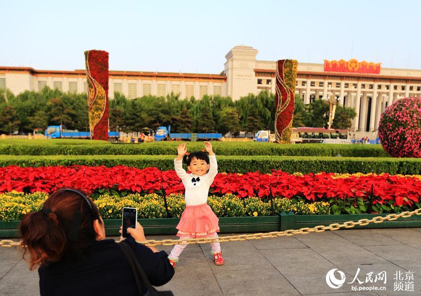 天安门广场,一位小朋友在已经布置完毕的绿地花卉前留影。